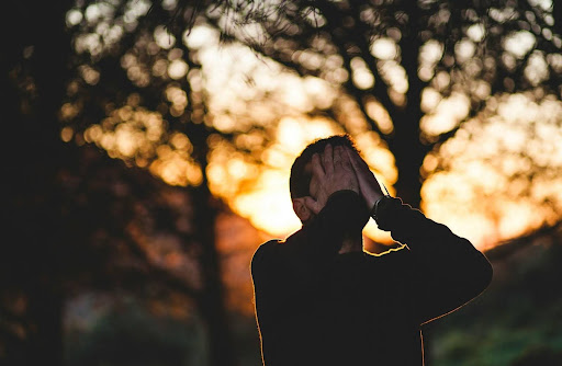 A visibly upset person holding their head outdoors at sunset - visual representation of when stress triggers health risks during recover